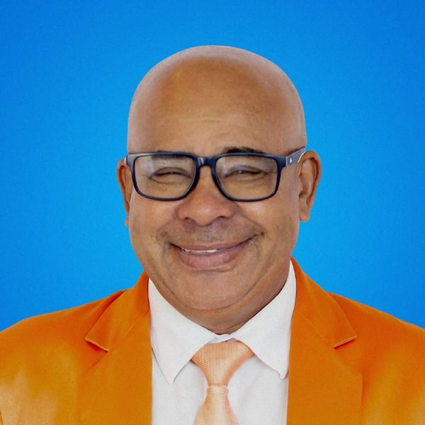 Retrato de Romério Duarte, de terno laranja e óculos, sorrindo.